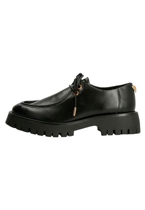 Chaussure noire en cuir à lacets avec semelle épaisse à crampons et œillets dorés, vue de côté sur fond blanc.