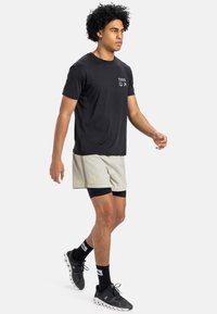 Černé tričko s krátkým rukávem a kapsou, spárované s světlými šedými šortkami se logem a bočním švem, obuté s černými sportovními botami.