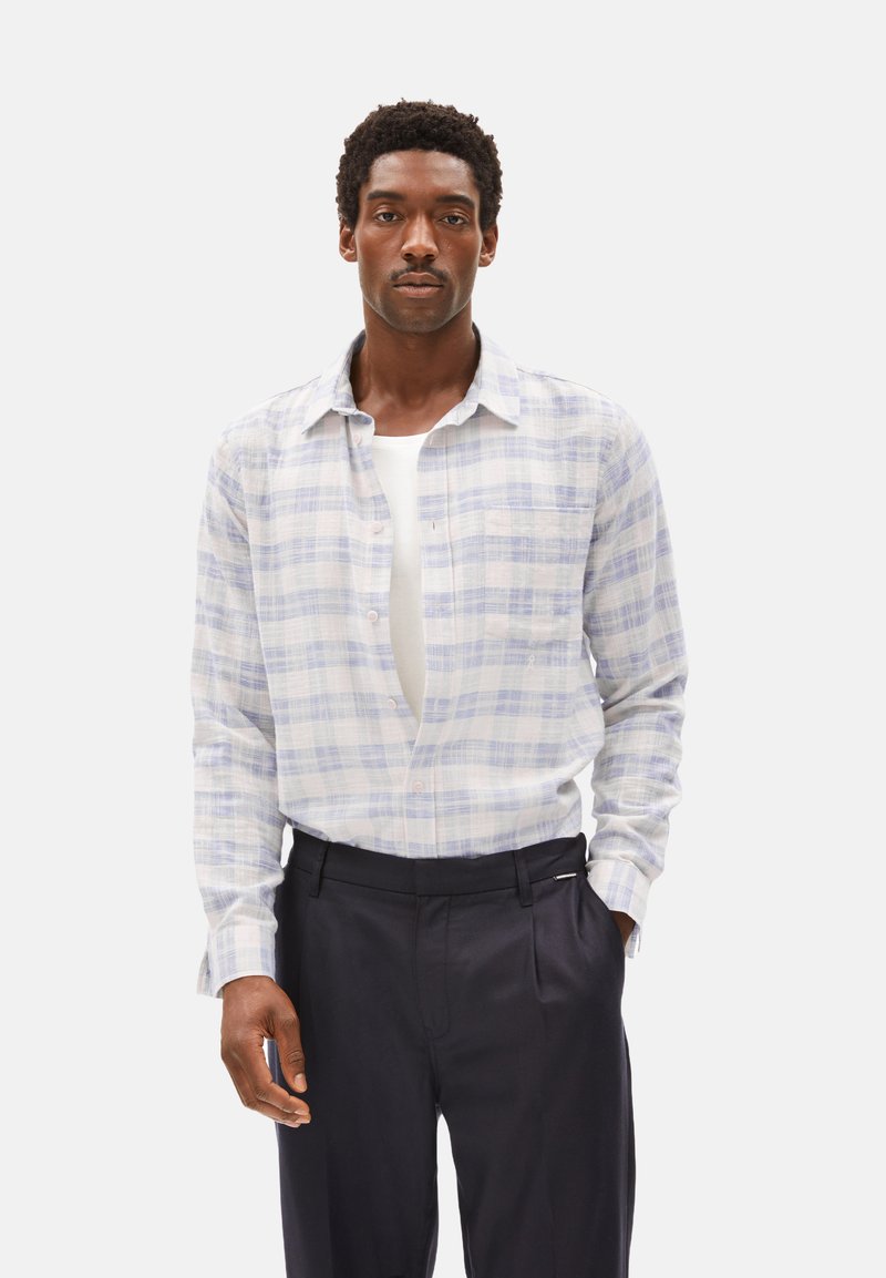 Camicia a quadri di colore azzurro chiaro e bianco, con colletto normale e maniche lunghe. Abbinata a pantaloni scuri su misura.