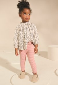Licht bloemenpatroon blouse met pofmouwen, gecombineerd met roze gestreepte leggings en beige instapschoenen met decoratieve accenten.