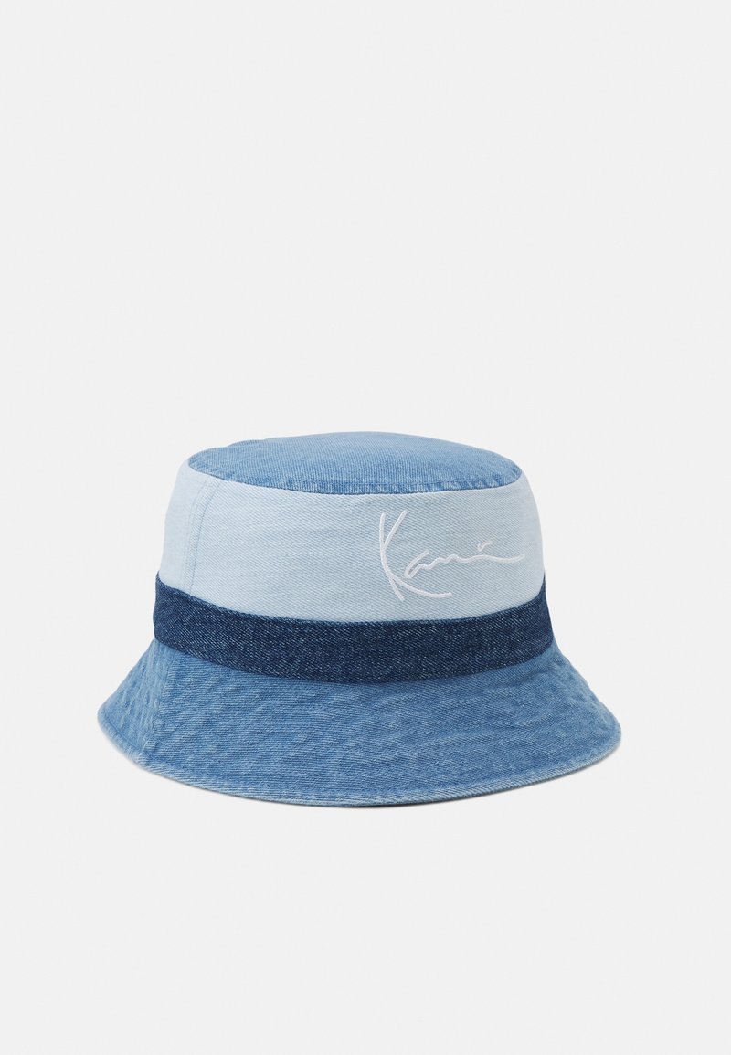 Chapeau bob en jean avec des panneaux bleu clair et bleu foncé, doté d'une bande bleu foncé et d'une signature blanche brodée sur le côté.
