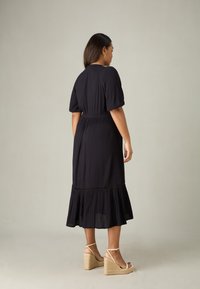 Svart, mjuk, flödande midi-klänning med korta puffärmar, cinchad midja och tiered fåll. Bärs med tan wedge sandaler med ankelremmar.