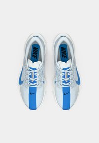 Par nogavic v beeli in modri barvi Nike za tek s vezalkami, modrim navpičnim trakom ter logotipi Nike znotraj in ob straneh.