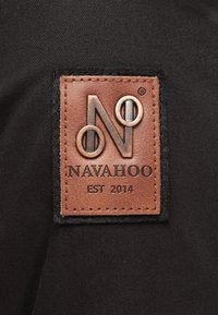 Dark fabric featuring a rectangular leather patch embossed with a logo, brand name "NAVAHOO," and "EST 2014" in contrasting colors.