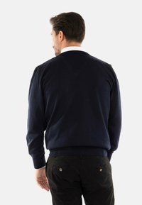 Maglione blu navy con maniche lunghe e collo a girocollo a coste, realizzato in un tessuto morbido, indossato sopra pantaloni neri.