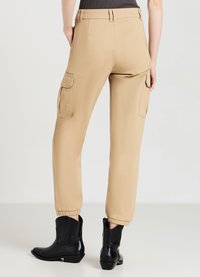 Beige Cargo-Hosen mit Seitentaschen, schmal zulaufenden Bündchen und einer glatten Textur, kombiniert mit schwarzen Stiefeln mit niedrigem Absatz.
