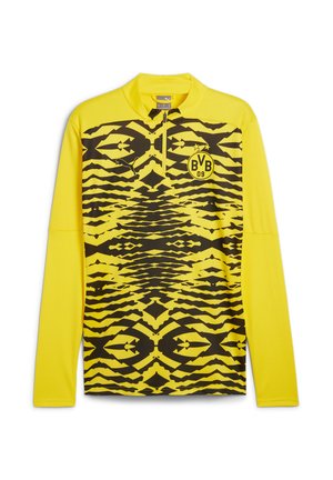 Gelbes langärmeliges Sportshirt mit einem halben Reißverschluss am Kragen, das ein auffälliges schwarzes Zickzackmuster und ein kreisförmiges Logo auf der Brust aufweist.