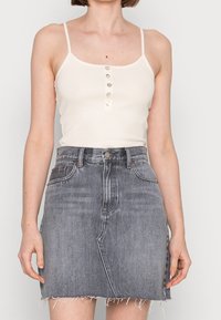 Débardeur blanc côtelé avec un devant boutonné, associé à une jupe en denim gris avec un ourlet effiloché et une silhouette ajustée.