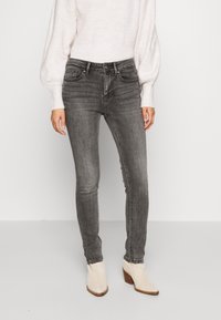 Jeans ajustados gris con un acabado desgastado, combinados con un suéter de punto ligero. Tela texturizada y diseño de cintura alta. Botas beige hasta el tobillo.