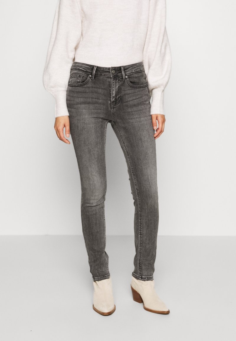 Jeans ajustados gris con un acabado desgastado, combinados con un suéter de punto ligero. Tela texturizada y diseño de cintura alta. Botas beige hasta el tobillo.