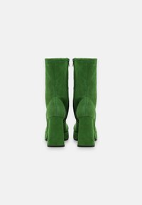 Bottines en suède vert avec un embout carré, un talonBloc et des fermetures éclair sur les côtés. Texture lisse et design haut pour couvrir la cheville.