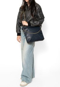 Borsa a tracolla in pelle trapuntata blu navy con catena dorata, caratterizzata da una forma rettangolare e una superficie liscia. Indossata in modo casual con jeans azzurri.