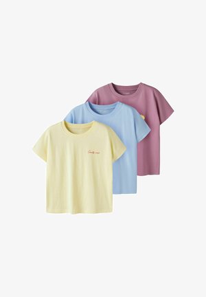 Trzy krótkie koszulki z okrągłym dekoltem w pastelowym żółtym, niebieskim i fioletowym kolorze, warstwowane z minimalistycznymi napisami i graficznymi detalami na piersi.