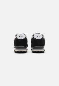 Zapatillas de running de ante negro y malla con una entresuela gris y suela exterior texturizada en negro, con sutiles acentos de logo en el tacón.