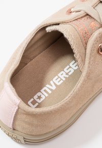 Beige suede sneaker met een textuur aan de binnenkant, een roze accent op de hak en een witte "CONVERSE" logo op de binnenzool.