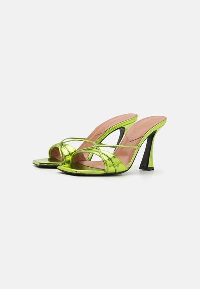 Grüne metallische High-Heels mit gekreuzten Riemen und offenen Zehen. Der Absatz ist schlank und spitz zulaufend, was einen Kontrast zur cremefarbenen Innensohle bildet.