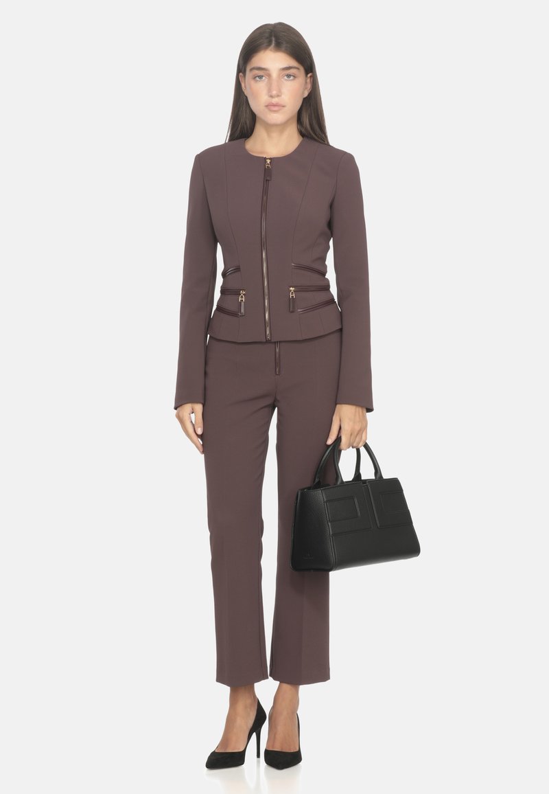 Dopasowana bordowa marynarka z zamkiem błyskawicznym i złotymi akcentami, w komplecie z dopasowanymi spodniami oraz usztywnioną czarną torebką. Zamszowe czarne szpilki.