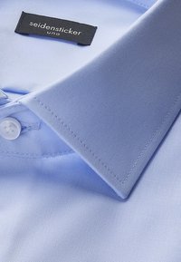 Jasnoniebieska koszula z kołnierzykiem wykonana z gładkiej tkaniny, z białym guzikiem i metką z napisem "seidensticker uno". Widoczny starannie wykonany szew.