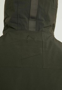 Ciemnozielona, wodoodporna kurtka z kapturem, wyposażona w przeszywane akcenty i pionowy pasek parciany. Gładka tekstura, minimalistyczny design.