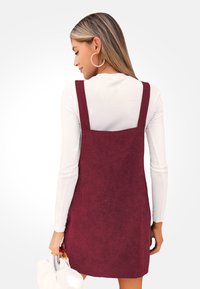 Bordeaux ribfluwelen jurk met brede bandjes en een vierkante halslijn, gecombineerd met een witte langslovige top en een witte tas.