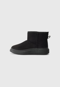 Bottes noires jusqu'à la cheville avec une tige en daim doux, un bout arrondi et une semelle en caoutchouc texturée. Elles présentent un collier court élastiqué et une boucle à l'arrière.