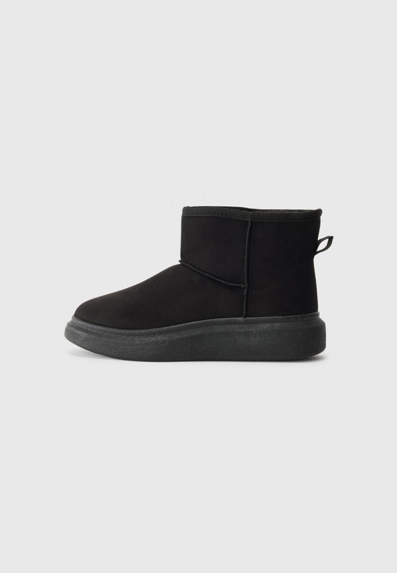 Bottes noires jusqu'à la cheville avec une tige en daim doux, un bout arrondi et une semelle en caoutchouc texturée. Elles présentent un collier court élastiqué et une boucle à l'arrière.