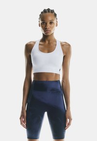 Top deportivo blanco con un escote amplio, combinado con pantalones cortos de ciclismo de tiro alto en azul oscuro que presentan una textura suave y costuras mínimas.