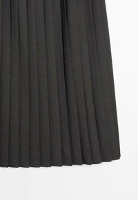 Sort plisseret nederdel lavet af et struktureret stof med markante, jævnt fordelt folder. Nederdelens kant er lige og slutter i midt-længde.