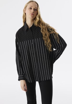Zwarte button-up shirt met een stippenpatroon op de bovenhelft en verticale strepen op de onderhelft. Lange mouwen, relaxed fit, zijsplit aan de zoom.