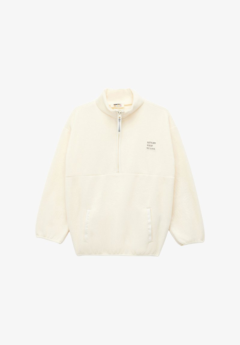 Pullover in pile color crema con colletto alto, zip frontale a metà e due tasche frontali. Presenta una piccola scritta stampata sul petto.