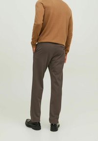 Hnědý svetr spojený s tmavě šedými kalhotami s bočními kapsami a zadní kapsou na knoflík, zobrazený zezadu. Černé boty doplňují vzhled.