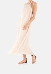 Beige halterjurk met een vloeiende uitstraling, gemaakt van lichtgewicht stof. Gecombineerd met platte sandalen met een zwarte enkelband en beige accenten.