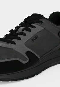 Gros plan d'une basket noire et grise avec des lacets noirs et le nom de la marque BOSS embossé sur le panneau latéral.