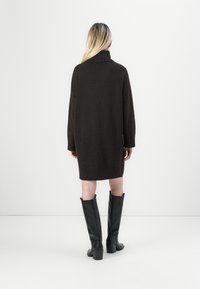 Neulemekko, jossa on korkea kaulus, pitkät hihat ja sivuhalkiot. Yhdistetty mustiin polvipitkiin saappaisiin, joissa on paksu korko.