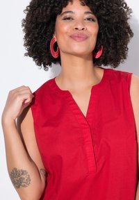 Blusa rossa senza maniche con scollatura a V, realizzata in tessuto morbido. Caratterizzata da linee pulite e un design semplice.