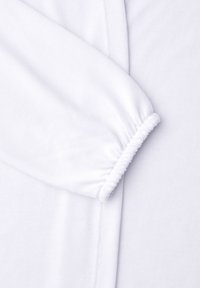 White long-sleeve garment with elastic cuff detail, showing fabric texture and seam on a smooth white background.