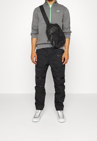 Šedá mikina na zip, černé cargo kalhoty s akcenty a kapsami, černá crossbody taška a šedé a bílé tenisky.