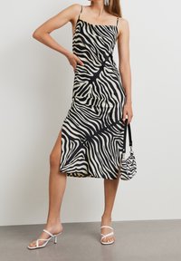 Mustavalkoinen seeprahiharaidallinen mekko, jossa on spagettiolkaimet, reisikorkea halkio, sileä pinta, yhdistettynä yhteensopivaan mini-laukkuun ja valkoisiin korkokenkiin.