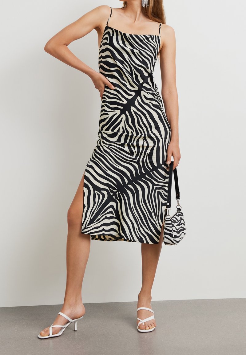 Mustavalkoinen seeprahiharaidallinen mekko, jossa on spagettiolkaimet, reisikorkea halkio, sileä pinta, yhdistettynä yhteensopivaan mini-laukkuun ja valkoisiin korkokenkiin.