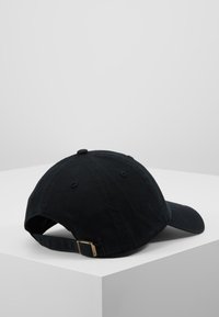 Gorra de béisbol negra de algodón con visera curva, correa de tela ajustable y hebilla metálica en la parte trasera. Textura suave y diseño clásico.