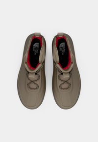 Et par beige høye The North Face sko med rød innvendig fôr og kryss-lisser, sett ovenfra på en hvit bakgrunn.
