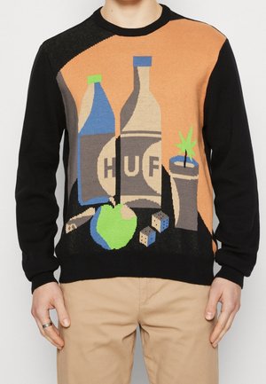 Sweter z abstrakcyjnym wzorem martwej natury przedstawiający dwie butelki, zielone jabłko, kości, zwiniętą papierosa oraz małą roślinę w doniczce.