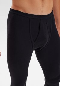 Black thermal leggings made of cotton blend, featuring a snug fit, elastic waistband, and reinforced stitching at the fly area.