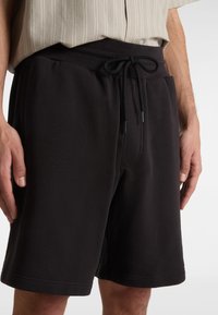 Pantaloni corti neri realizzati in tessuto morbido, con cintura elastica e coulisse, tasche laterali e dettagli di cucitura visibili.