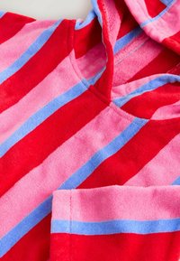 Poncho plażowe z frotté z czerwonymi, różowymi i niebieskimi pionowymi paskami oraz kapturem, złożone tak, aby pokazać szczegóły rękawa i dekoltu.