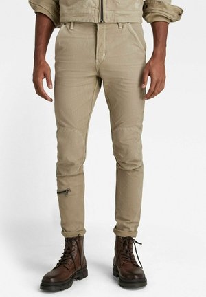 Pantalons cargo beige à jambe fuselée avec des patchs aux genoux, poche zippée sur la jambe inférieure et des détails cousus, fabriqués en tissu léger et durable.