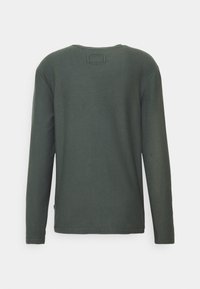 Koszulka z długim rękawem i okrągłym dekoltem w ciemnozielonym kolorze, wykonana z teksturowanej tkaniny. Na plecach znajduje się prostokątna metka z delikatnymi akcentami szwów.