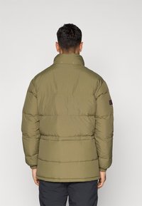 Jakna s puhavicama, visoki ovratnik, maslinasto zelena boja, kvadratni uzorak, elastični manžetni i mali logo na lijevoj rukavu.