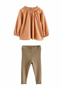 Blouse pêche avec imprimé floral et encolure froncée, associée à des leggings beiges côtelés offrant une coupe ajustée. Les deux présentent des textures de tissu douce.