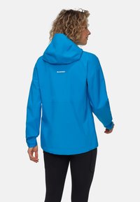 Blå vattentät jacka med huva, med en avslappnad passform, elastiska muddar och "MAMMUT"-logotypen på ryggen. Slätt, lätt material.